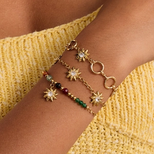 Elegant gold bracelet set with sun charms and beads worn on wrist with yellow knitwear