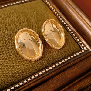 Macro detail of vintage gold oval stud earring displayed on a dark green knit frame