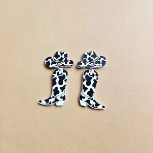 Detail of western cow print acrylic earrings featuring cowboy boot and hat charms