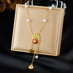 Detail of gold-plated necklace with ladybug, flower charms and pearl tassels on black silk