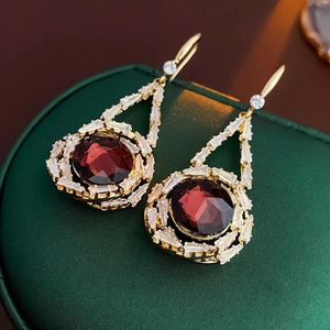 Detail of tear-drop earrings featuring dark red gemstones and white cubic zirconia