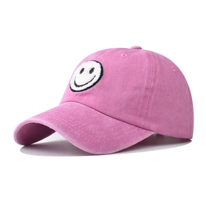 Close-up of pink washed baseball cap featuring a smiley face towel embroidery detail
