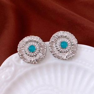 Close-up of flower-shaped earrings with blue center bead and white zircon stones on a dish