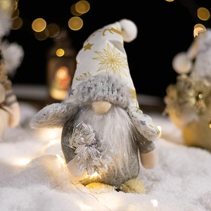 Christmas gnome plush doll with gray body and gold star hat on snow with warm lights