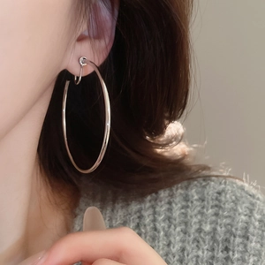 Side view detail of a large silver minimalist circular clip-on earring worn on the ear