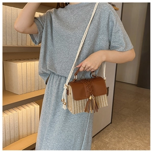 Detail of woven straw crossbody bag with brown leather trim and tassel on a model