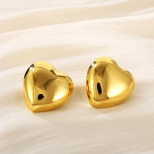 Poliert goldene Herzstecker aus Edelstahl auf elegantem beigefarbenem Seidenstoff liegend