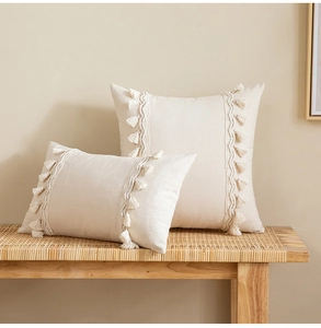 Detail of cream tassel cushions on rattan bench with woven linen texture and bohemian style