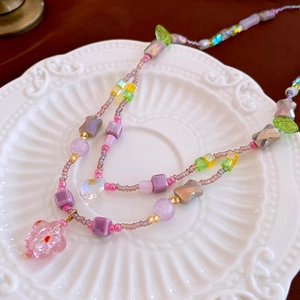 Detail of beaded floral necklace with pastel glass charms and leaf elements in a ceramic bowl