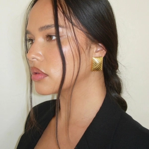 Detail shot of gold rectangular earrings with elegant diagonal striped texture on a model