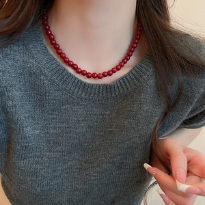Close-up of minimalist deep red glass bead necklace worn on a dark grey sweater
