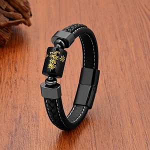 Close-up of braided black leather bracelet with golden engraved mantra on black steel bead