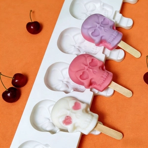 Moule en silicone pour 4 glaces en forme de crâne avec bâtonnets sur fond orange texturé