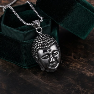 Detailed close-up of ethnic Buddha head pendant in vintage silver on green velvet