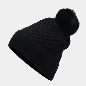 Detailed view of black honeycomb knit hat featuring a large soft faux fur pom-pom
