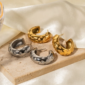 Close-up of gold and silver C-shaped earrings with heart texture on silk background