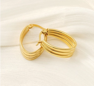 Detail of gold-plated triple hoop earrings resting on elegant white silk fabric