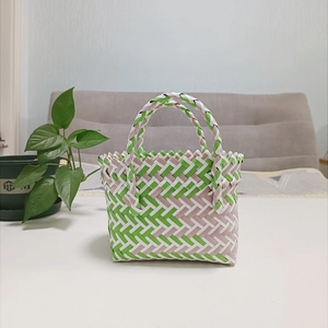 Detail of green and beige hand-woven basket bag showing intricate plaid texture on a table
