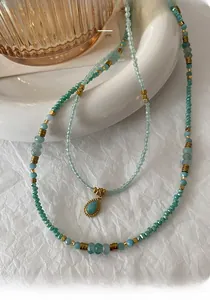 Detail of bohemian necklace with turquoise beads and gold teardrop pendant on white ceramic