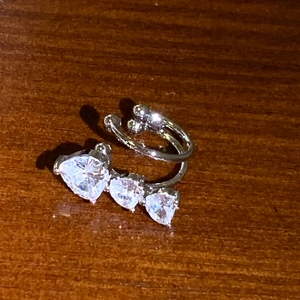 Vista detallada de un ear cuff plateado con circonitas de corazón para orejas sin agujero.
