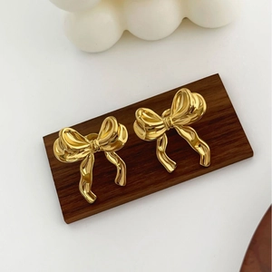 Boucles d'oreilles nœud dorées élégantes sur support en bois avec fond blanc minimaliste
