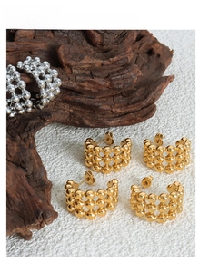 Detail shot of gold and silver beaded C-shape hoop earrings on textured wood