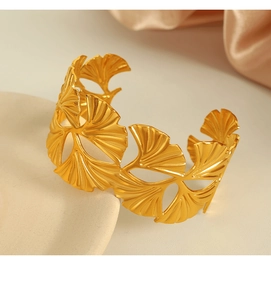 Detail of golden stainless steel bangle with hollow ginkgo leaf pattern on silk background