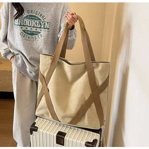 Detail of beige canvas tote bag with reinforced straps placed on a white suitcase
