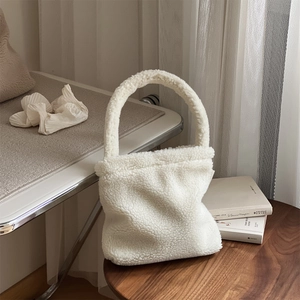 Close-up of white sherpa fleece handbag on wooden table with cozy neutral background