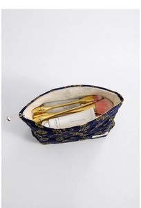 Detailed top view of navy velvet daisy makeup bag with gold embroidery and beauty items