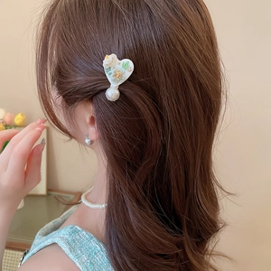 Détail de la pince à cheveux cœur avec fleurs et perle sur cheveux bruns