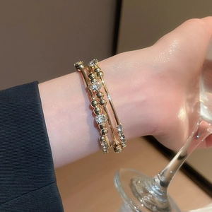 Detail of layered gold bangles with rhinestones worn by a model holding a glass