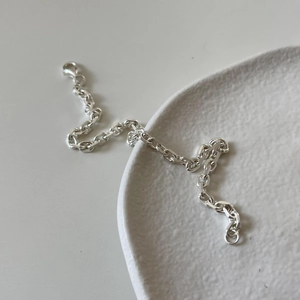 Macro view of sterling silver chain bracelet with lobster clasp on white ceramic plate