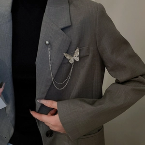 Detailed view of silver butterfly chain brooch with pearl accent on grey suit blazer