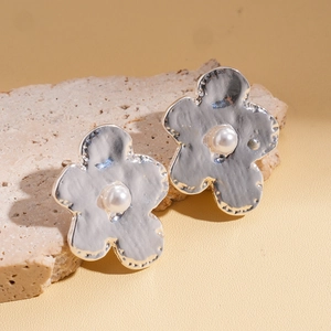 Detailed view of silver flower earrings with hammered texture and white pearl center