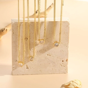 Detail view of four gold-tone necklaces with heart and teardrop zircon pendants on stone