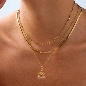 Close-up of triple layered gold cherry necklace with pink zircons on a model