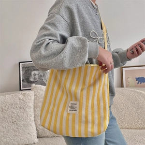 Dettaglio di una borsa a spalla in tela a righe gialle e beige con toppa in tessuto quadrata