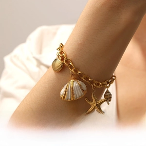 Close-up of gold stainless steel bracelet with starfish, seashell and conch charms on wrist