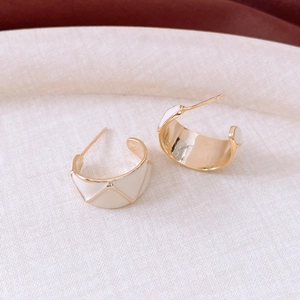 Macro shot of 18k gold vintage C-shaped earrings with cream enamel diamond pattern
