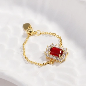 Macro detail of adjustable gold chain ring with square red gemstone and heart charm