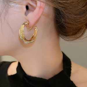 Close-up of elegant layered gold twisted hoop earrings worn by a model in soft lighting