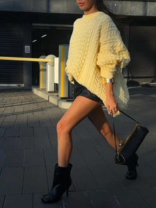 Detail of yellow chunky cable knit sweater worn with black leather shorts in city setting