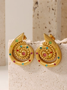 Detailed shot of gold spiral earrings with multi-colored crystals on a stone surface
