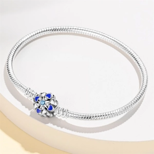 Macro detail of silver snake chain bracelet featuring a blue enamel flower bead and gemstone