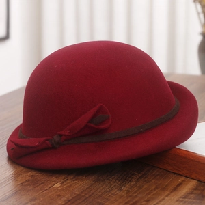 Close-up of dark red wool beret with brown ribbon bow on a rustic wooden surface