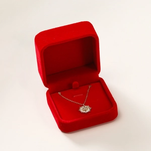 Red velvet jewelry box with a gold sunflower pendant necklace on white background