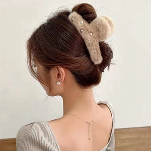 Detail view of a beige plush hair claw clip with pearl accents worn by a model