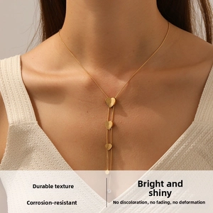 Detail of gold chain necklace featuring three matte heart pendants on a female model