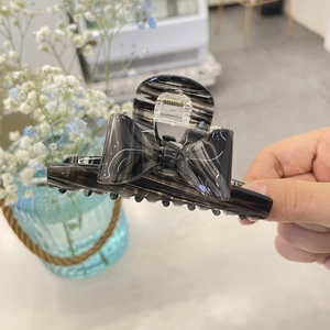 Black striped acrylic bow hair claw clip for women in a soft indoor setting